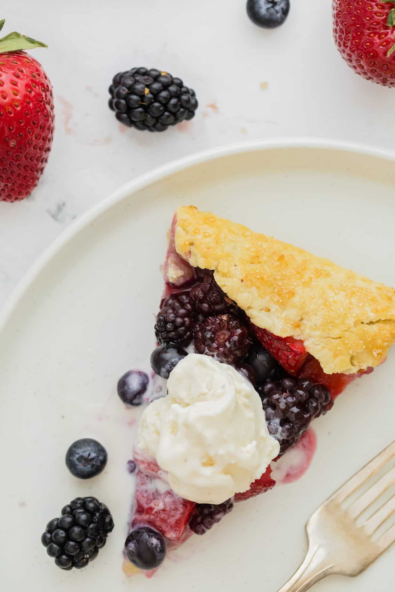Slice of berry galette on a plate, topped with a scoop of vanilla ice cream.