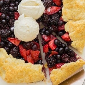 Berry galette, topped with two scoops of vanilla ice cream, one slice cut.