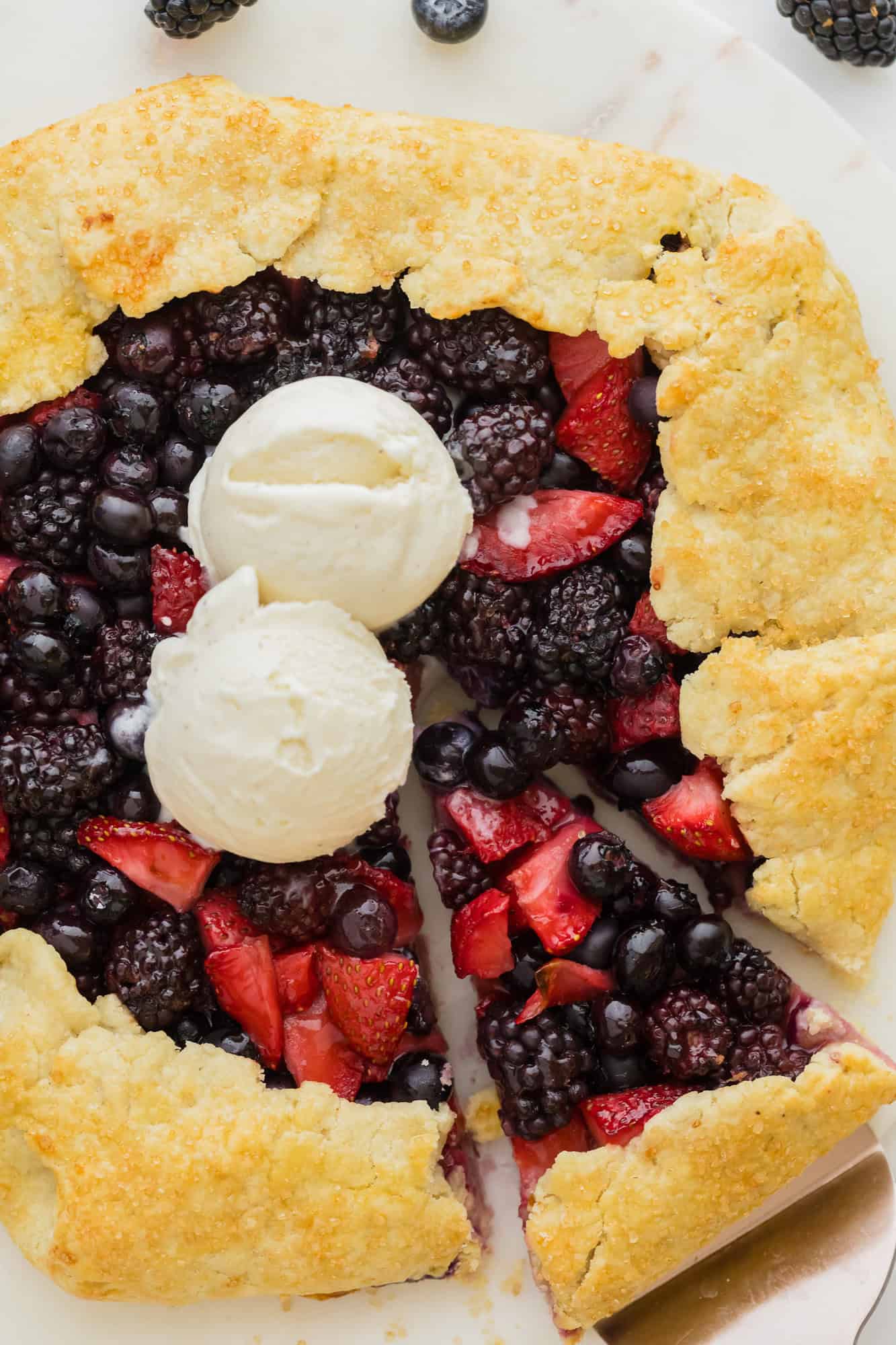 Berry galette, topped with two scoops of vanilla ice cream, one slice cut.