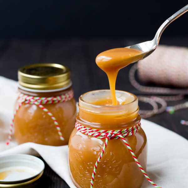 Caramel sauce on spoon being held over a jar.