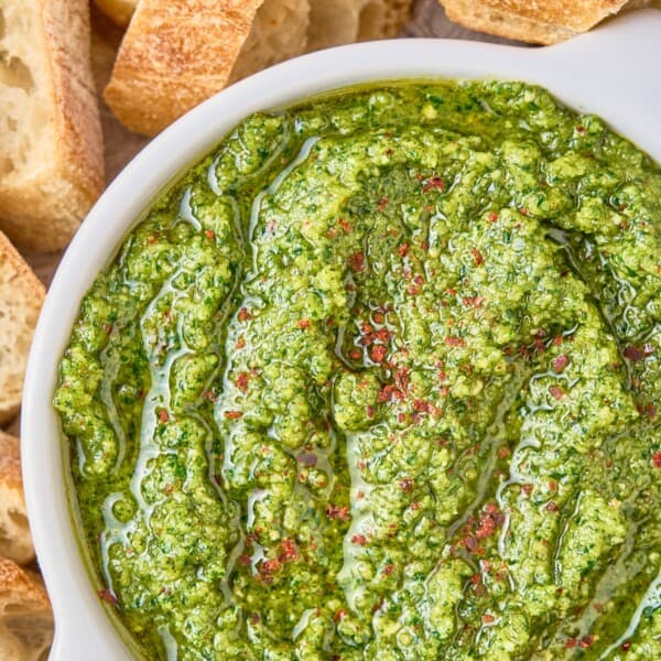 Cilantro pesto in a white bowl surrounded by slices of bread.