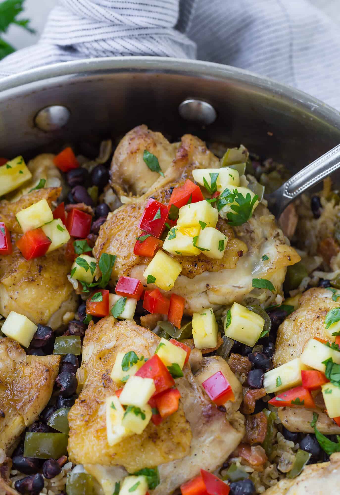 Cuban chicken thigh on a spoon in a pan, on a bed of rice.