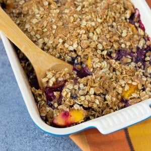 Peach blueberry crisp with a wooden serving spoon in it.