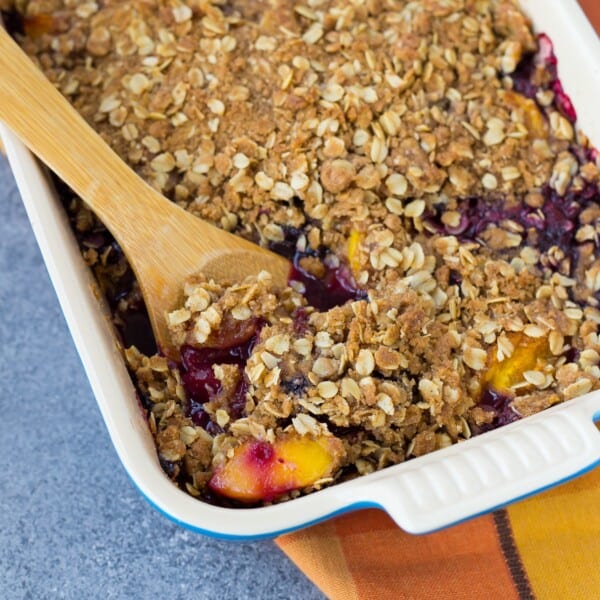 Peach blueberry crisp with a wooden serving spoon in it.