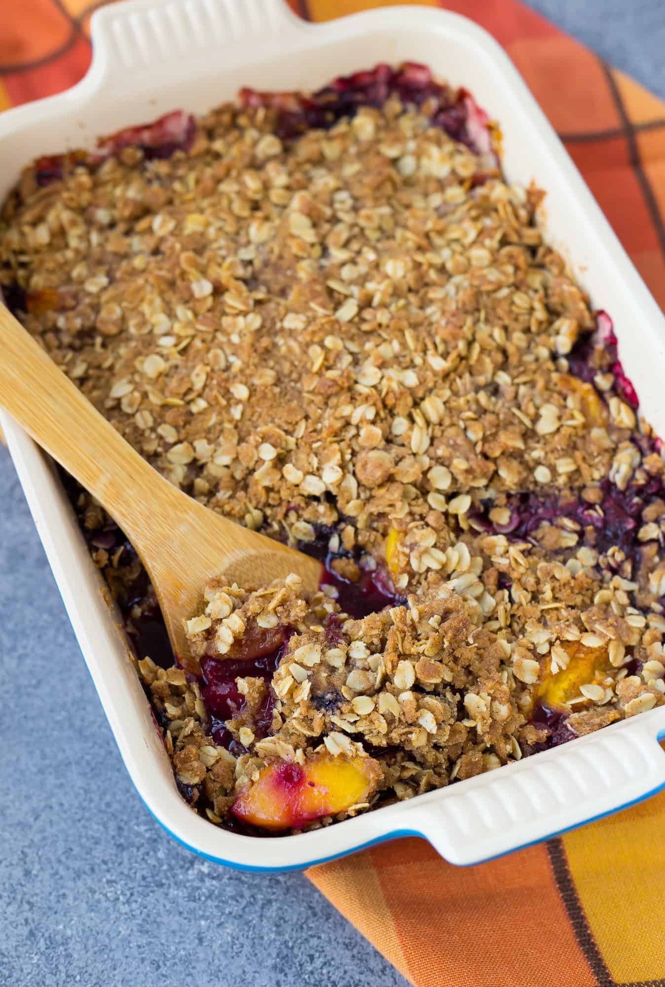 Peach blueberry crisp with a large wooden spoon in it.