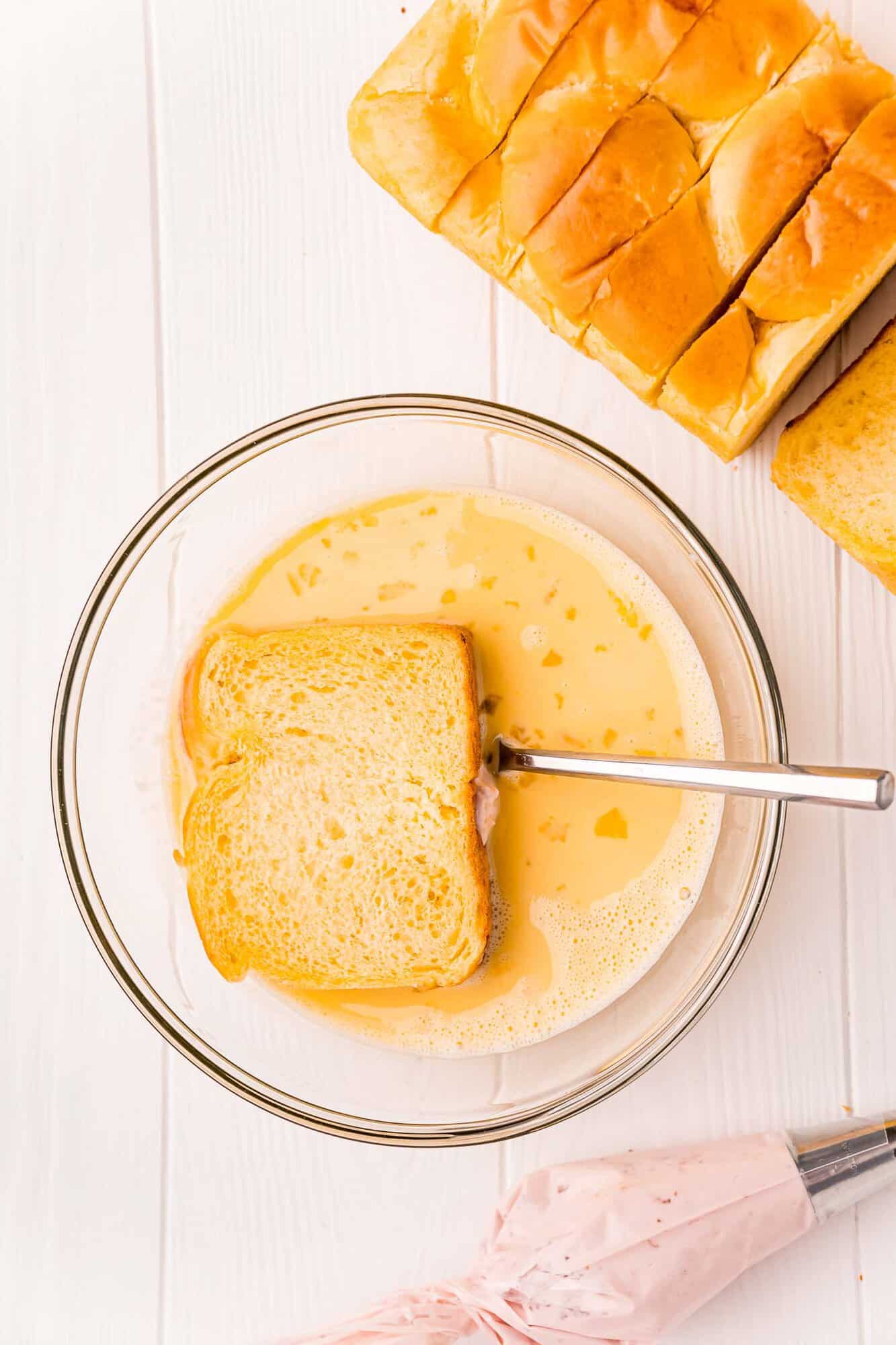 Bread being dipped in a bowl of egg mixture.