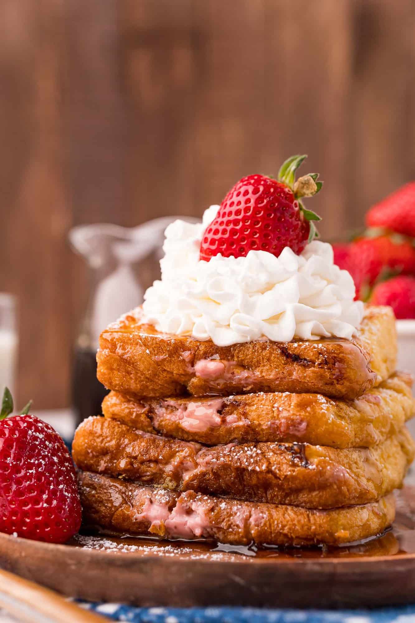 Stack of stuffed french toast topped with a strawberry and whipped cream.