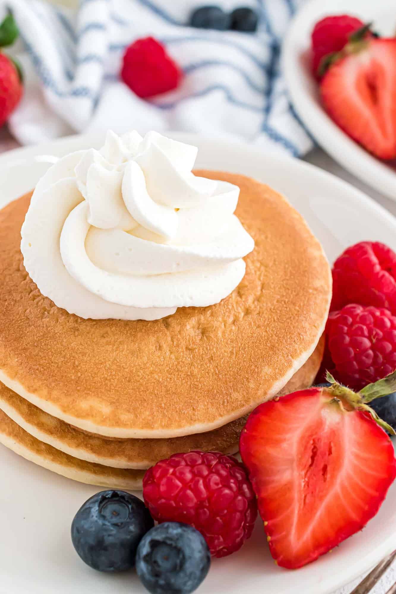 Whipped cream on a short stack of pancakes.