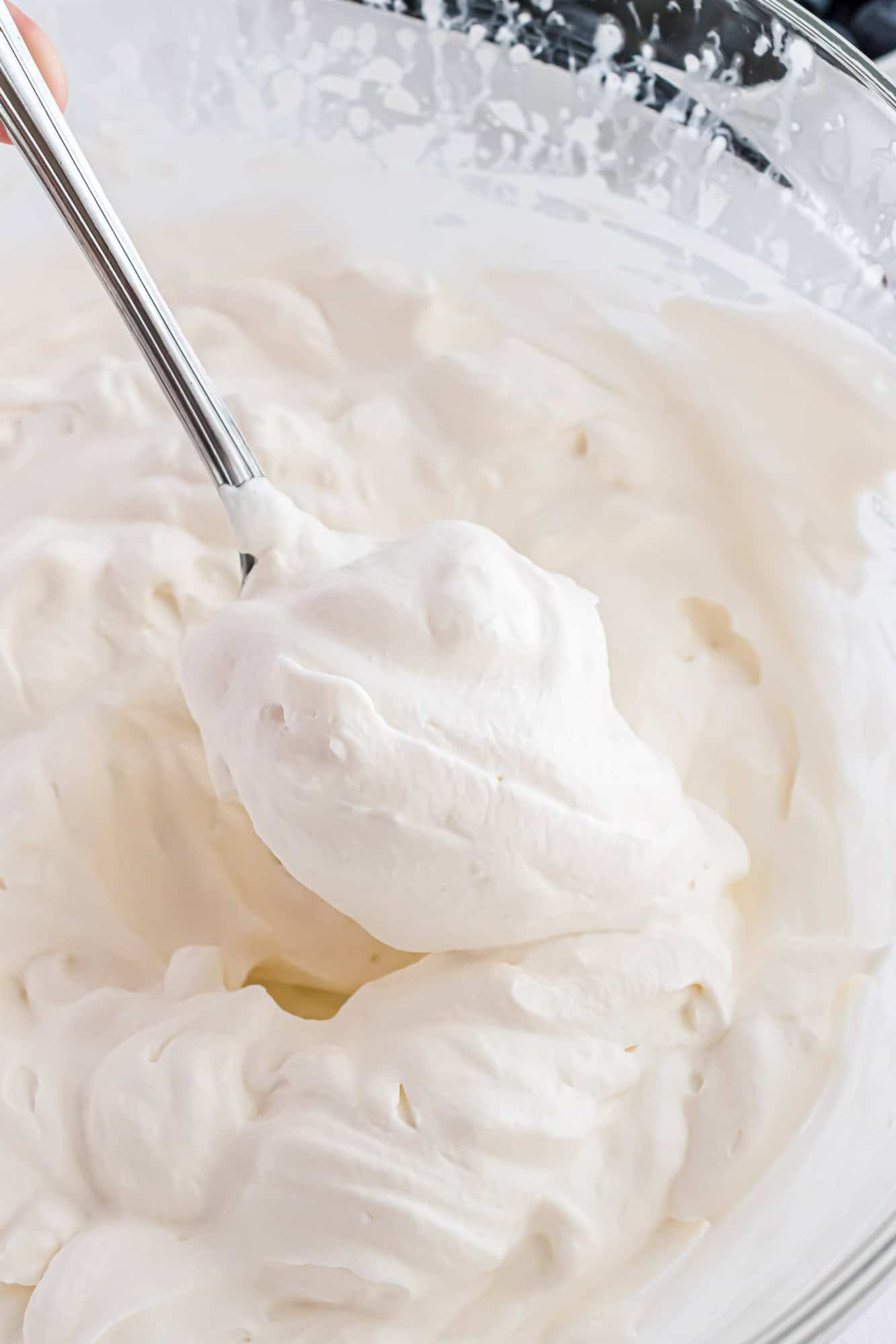 Freshly whipped cream, on a spoon, in a mixing bowl.