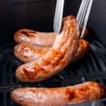 Air fryer brat being lifted out of the air fryer with tongs.