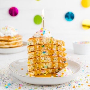 Stack of birthday cake pancakes, cut like cake, with a candle.