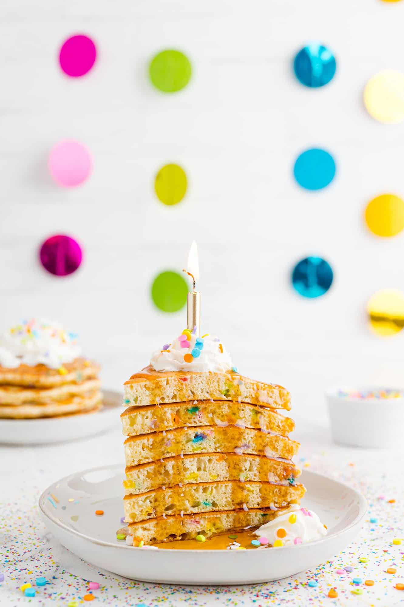Stack of pancakes cut into a wedge to look like a slice of birthday cake, topped with syrup.