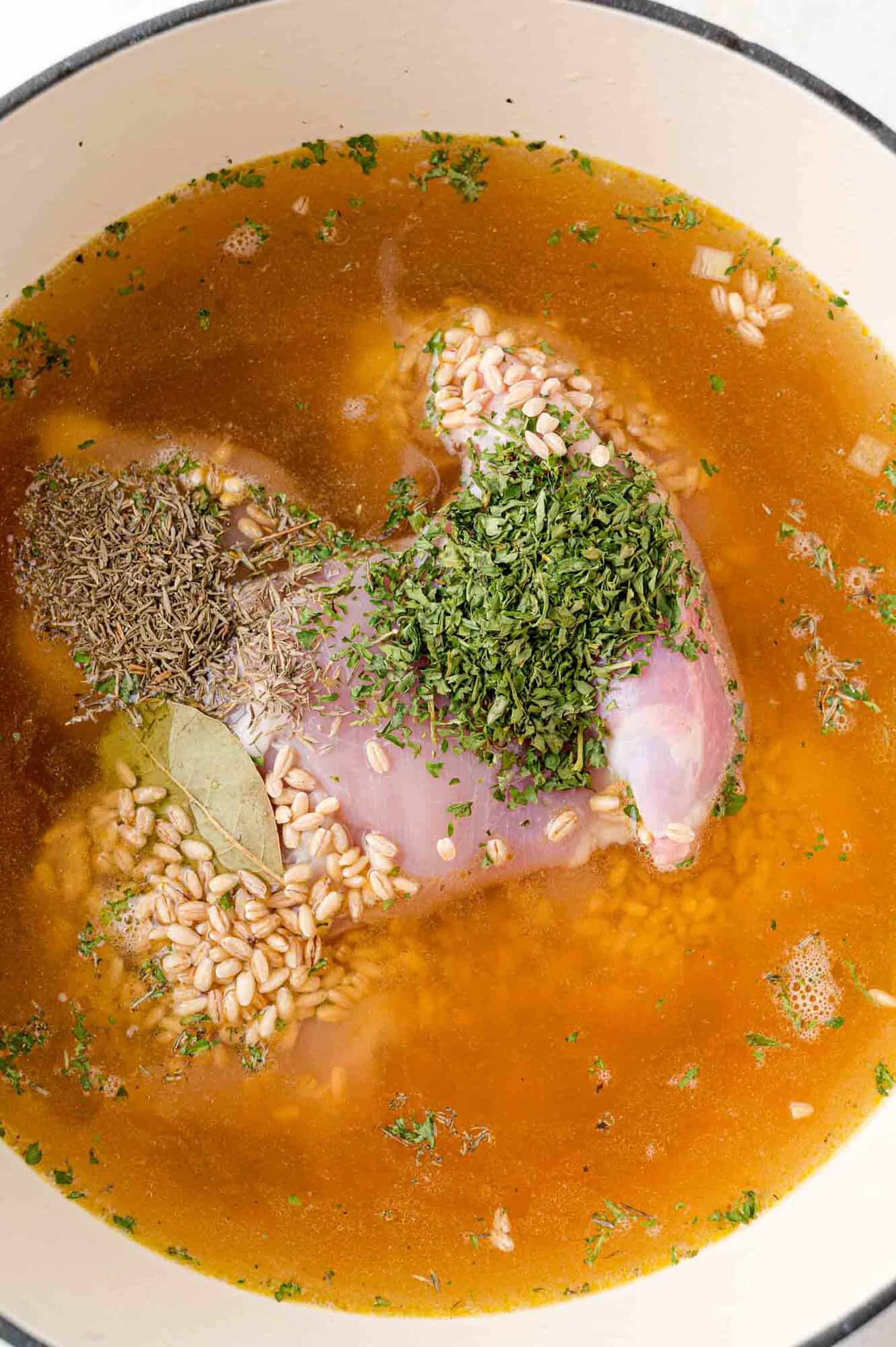 Additional ingredients being added to soup - barley, chicken, herbs.