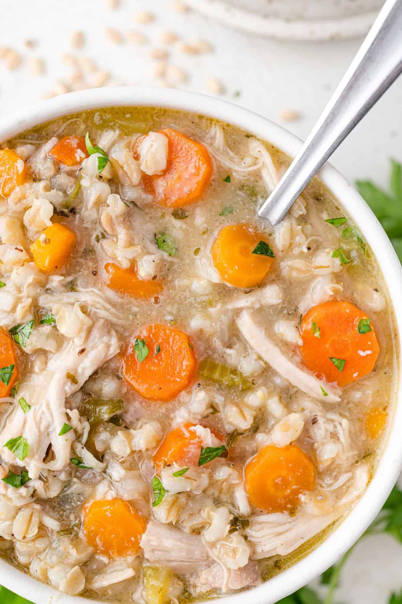 Overhead view of chicken barley soup in a white bowl with a silver spoon.