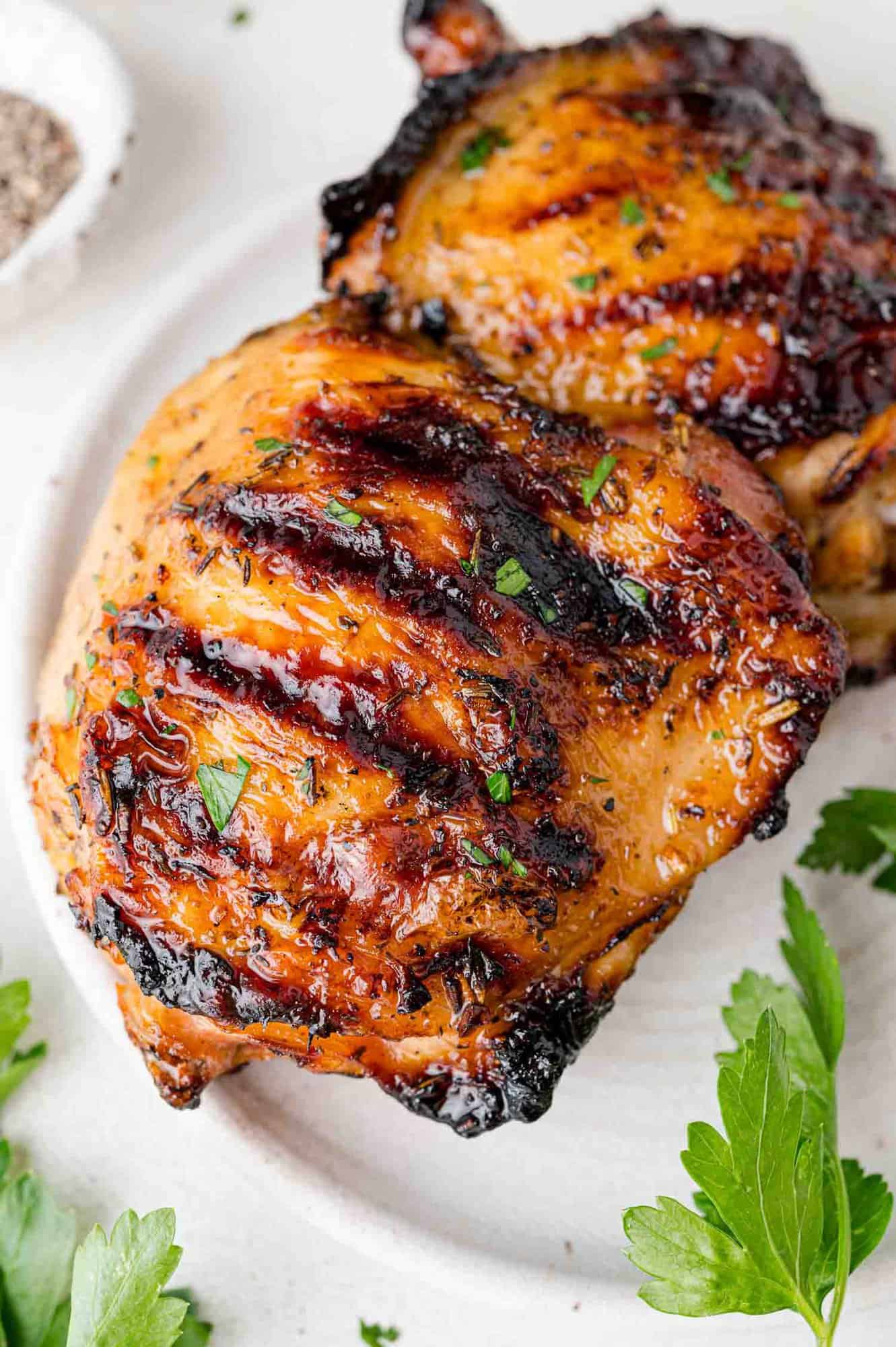 Close up of a grilled chicken thigh on a plate with another.