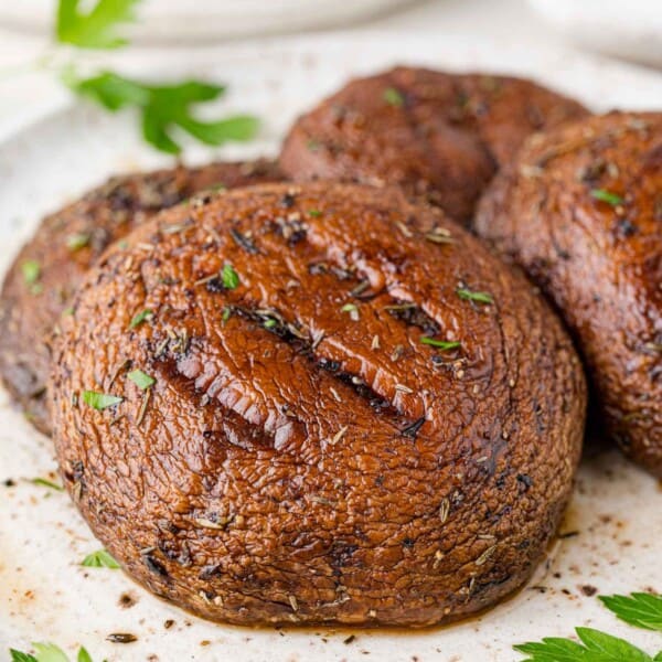 Grilled portobello mushrooms placed on a white plate and garnished with fresh parsley.