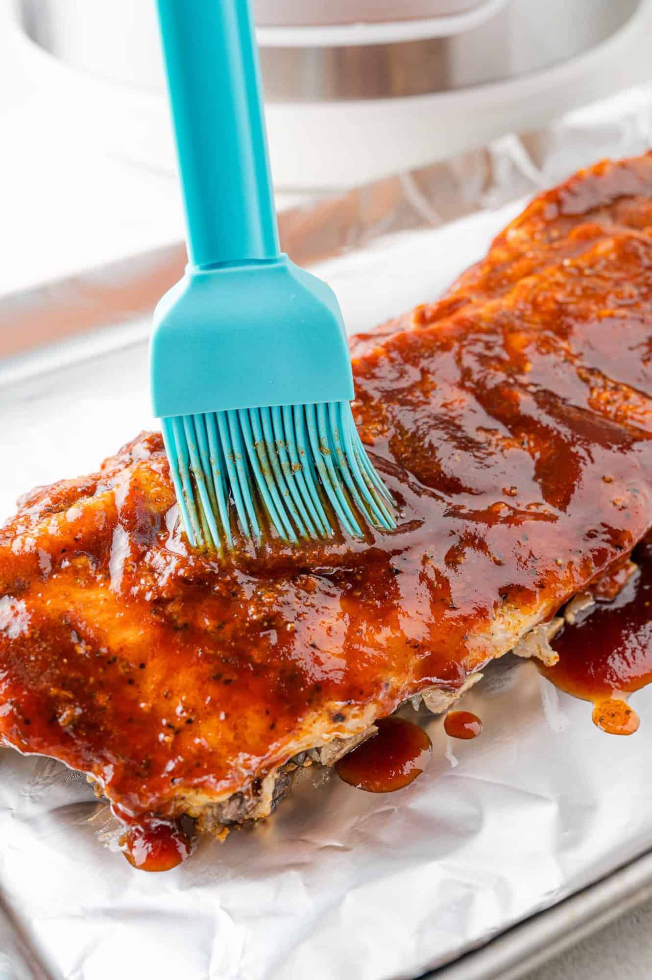 Cooked ribs being brushed with bbq sauce.