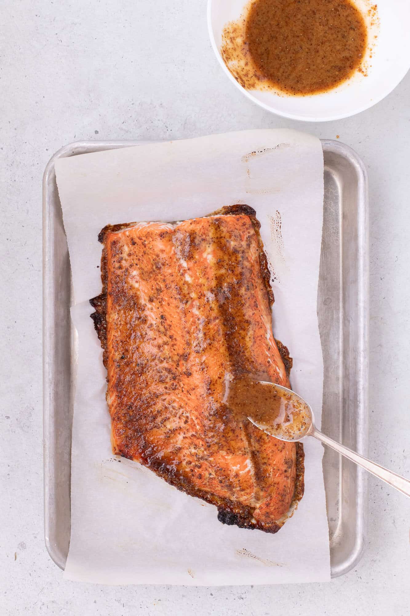 Additional glaze being added to partially baked salmon fillet.
