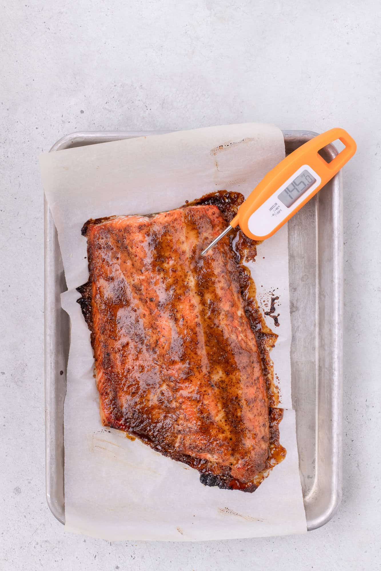 Temperature of salmon being checked with a thermometer that reads 145 degrees F.
