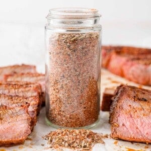 Jar of steak seasoning surrounded by cooked steak.