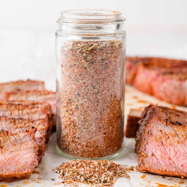 Jar of steak seasoning surrounded by cooked steak.
