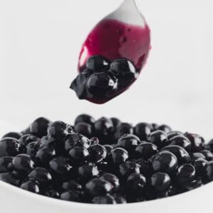 Blueberry sauce being scooped from a white bowl with a spoon.