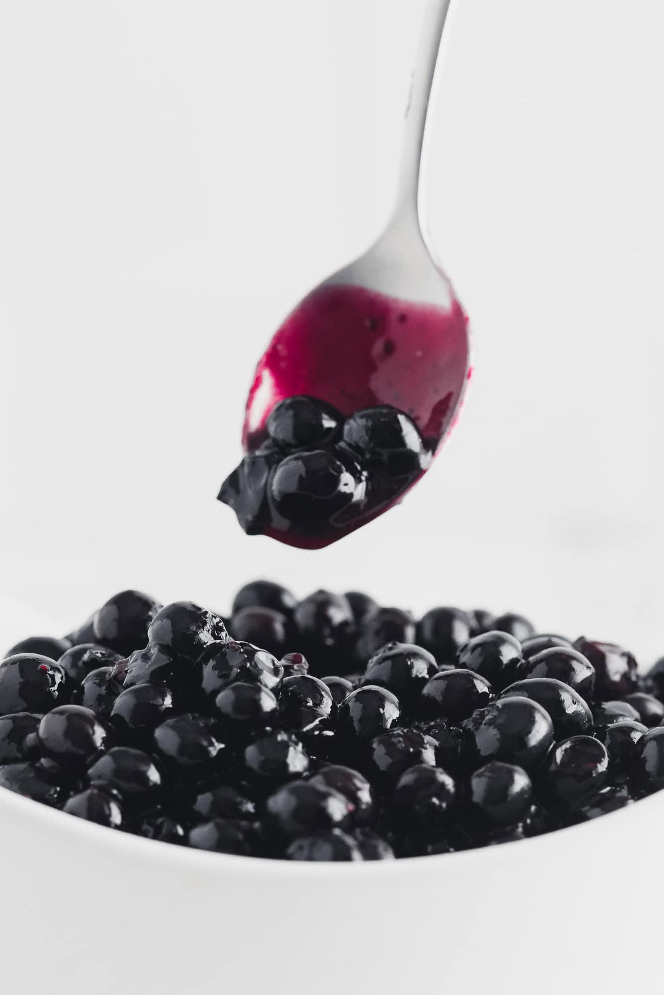 Blueberry sauce being scooped from a white bowl with a spoon.