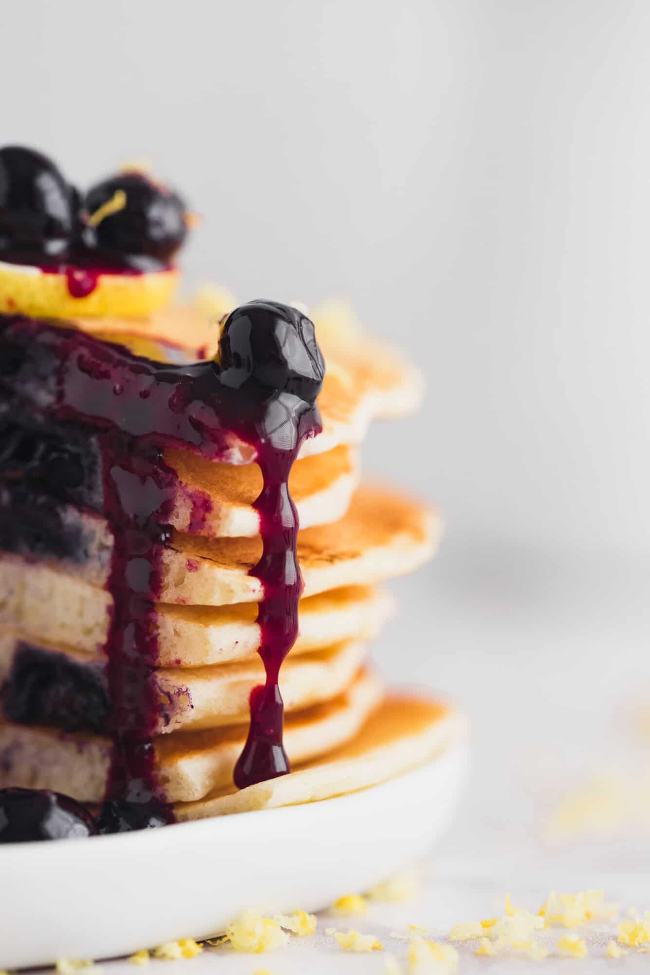 Homemade blueberry sauce dripping down the side of a tall stack of pancakes.