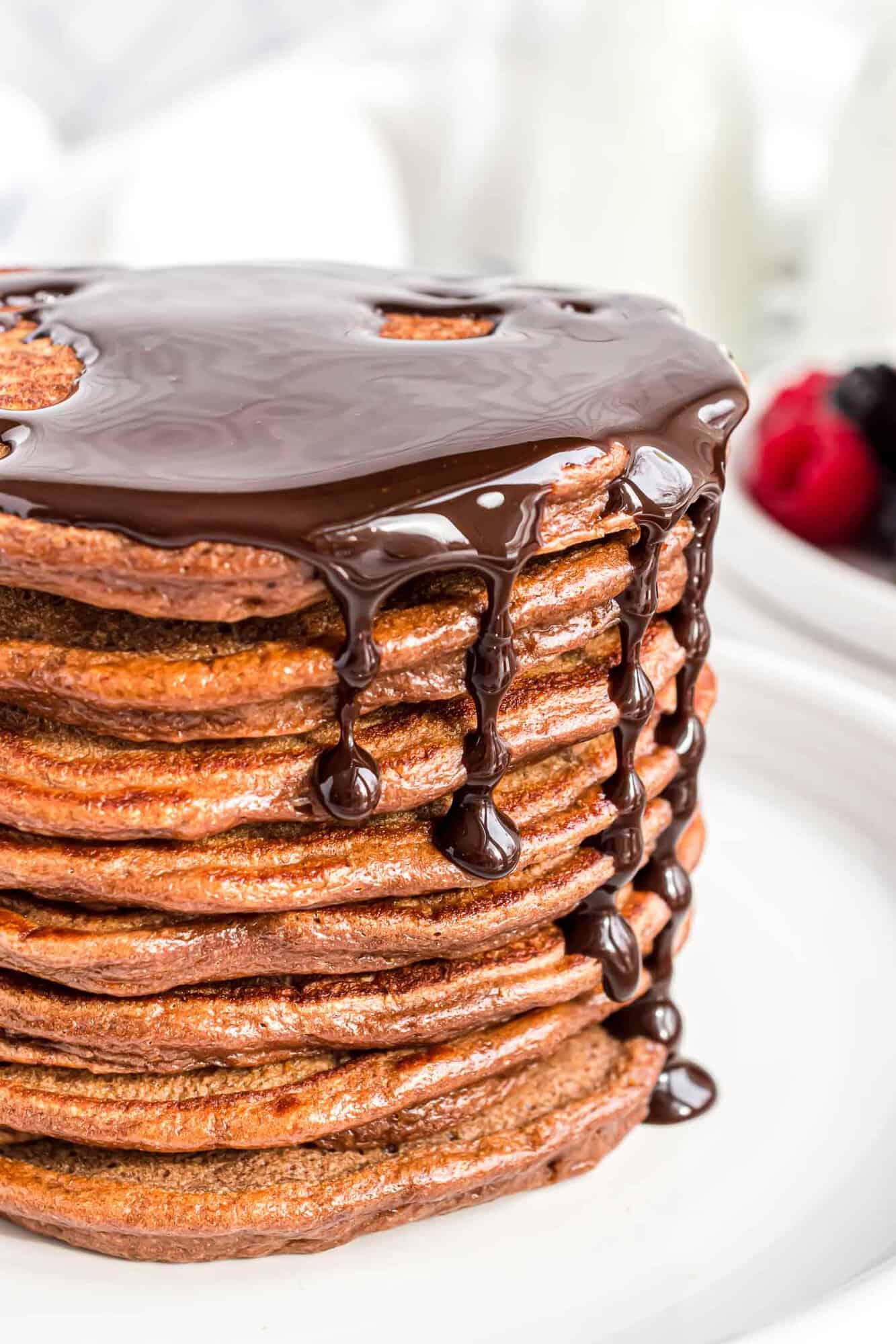 Stack of chocolate pancakes topped with chocolate syrup.