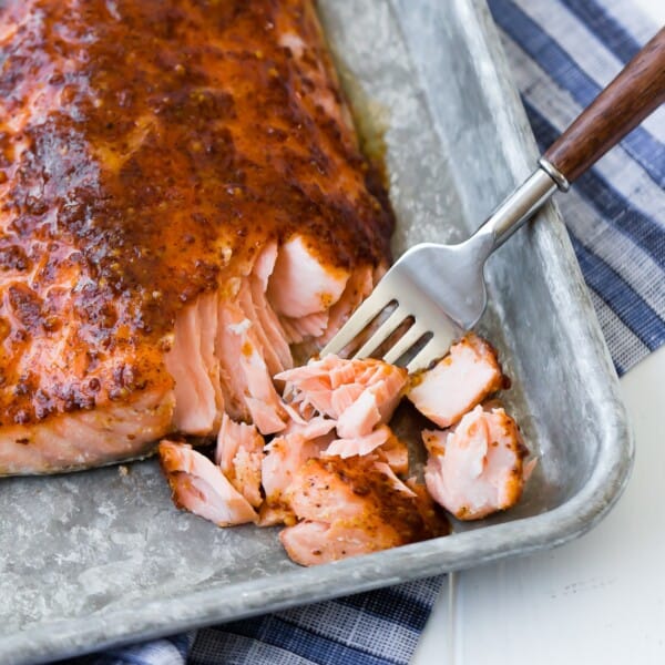 Maple mustard baked salmon on a sheet pan, being flaked with a fork.