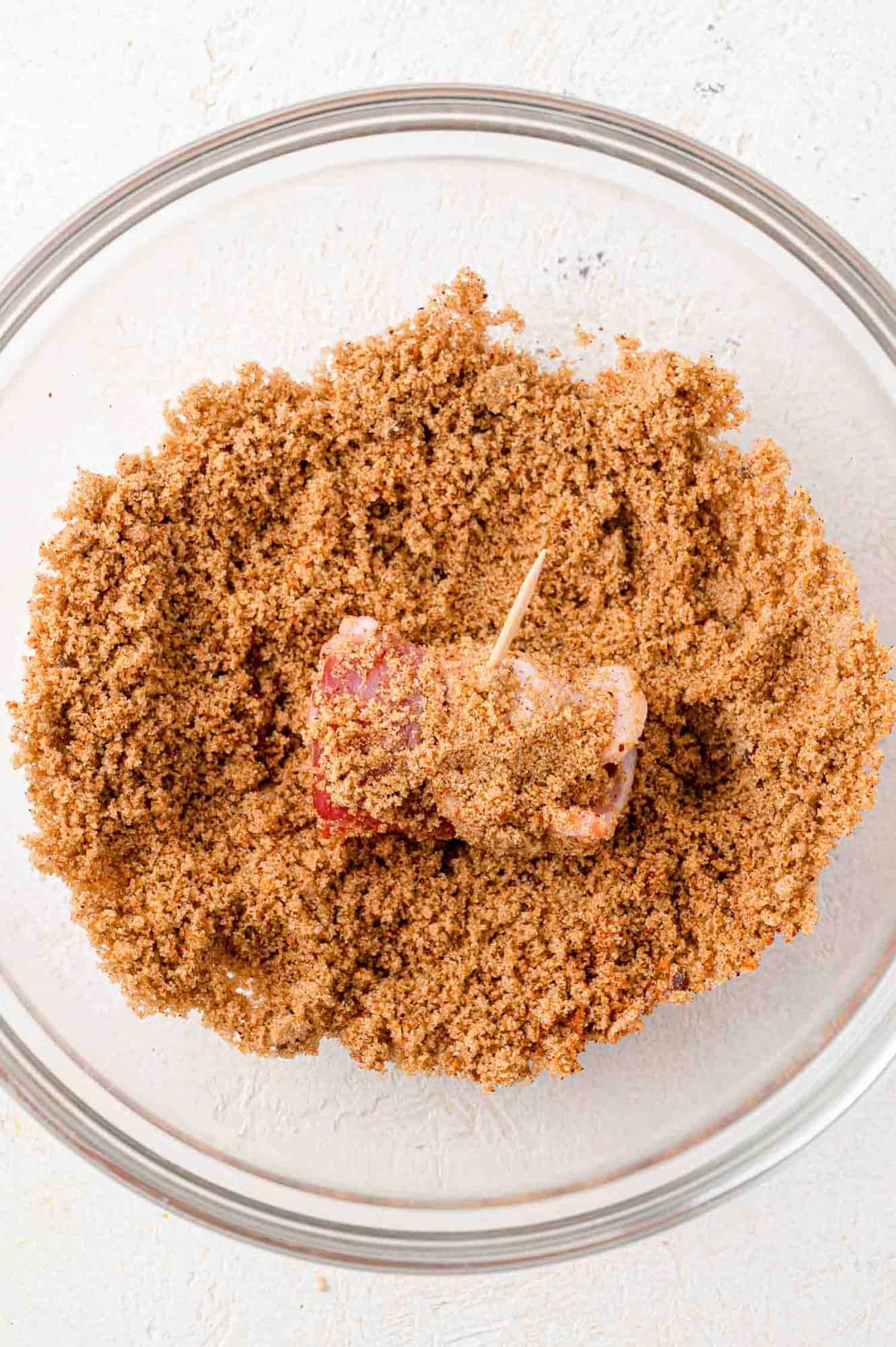 Bacon wrapped date being rolled in sugar spice mixture.