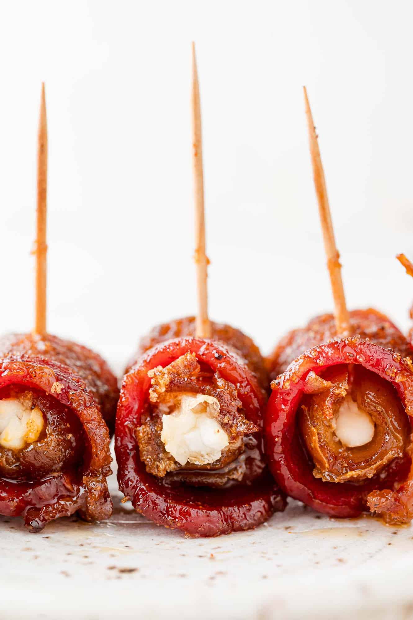 Three bacon wrapped dates on a plate, turned to show filling. 