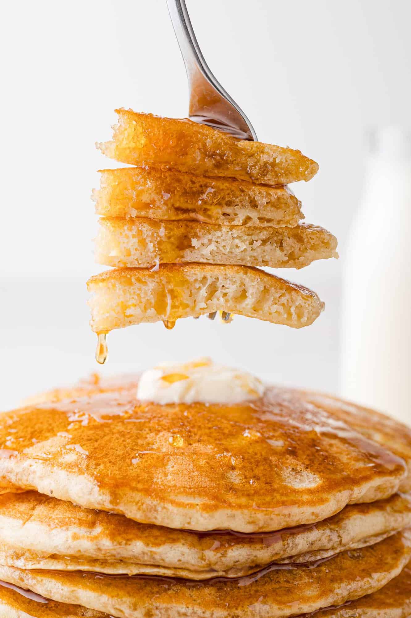 Buttermilk pancakes, cut and on a fork, showing texture. Syrup dripping off them.