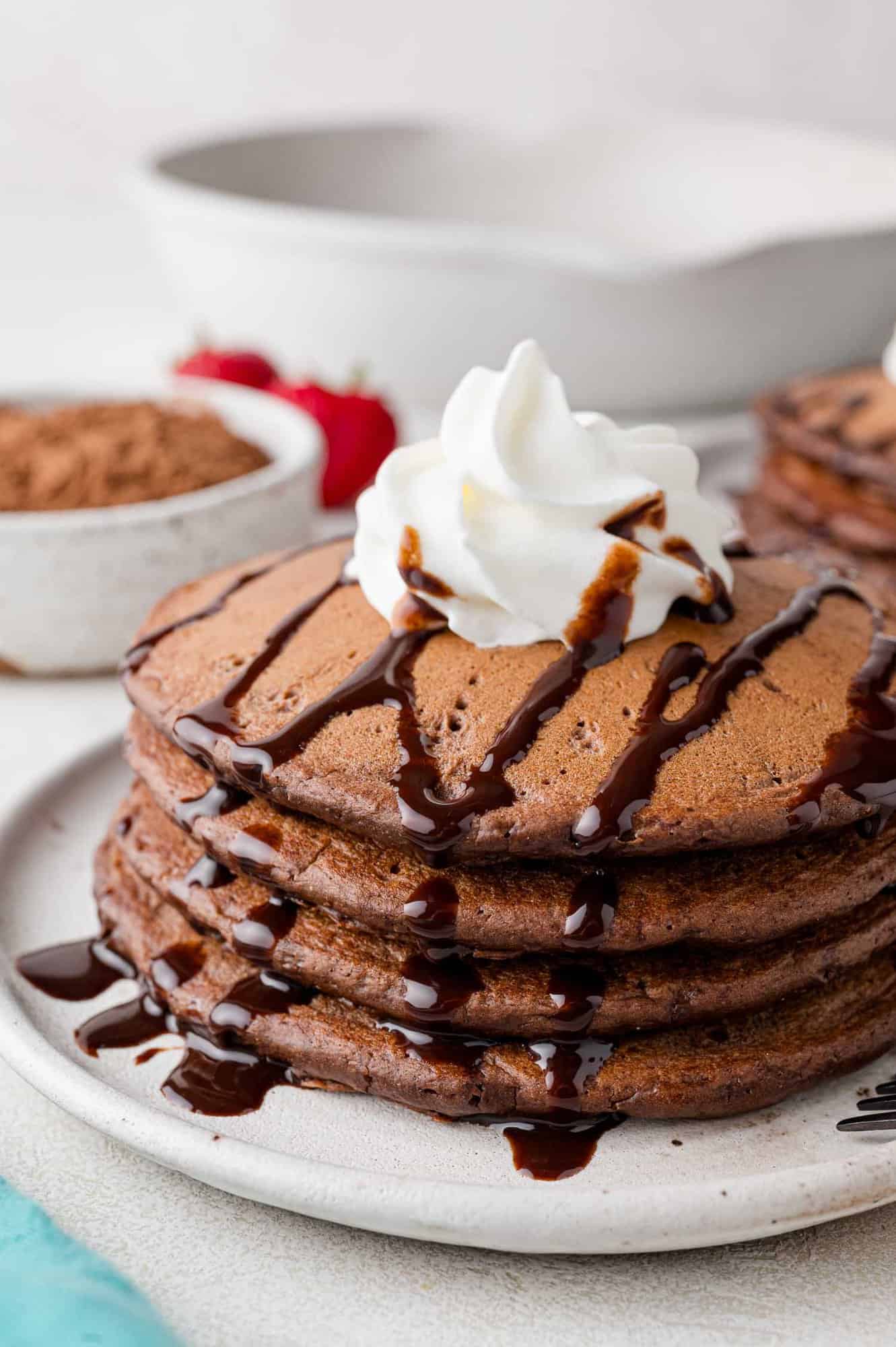 Stack of chocolate pancakes with chocolate syrup and whipped cream.