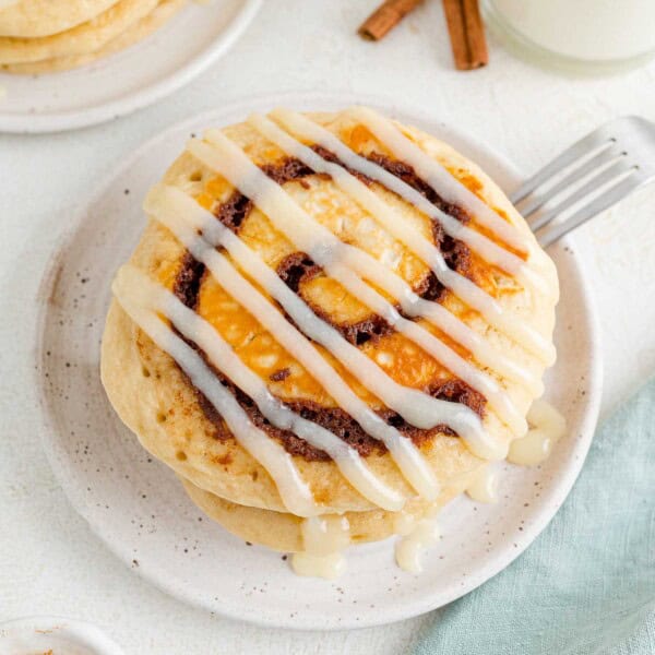 Small stack of cinnamon roll pancakes with icing drizzled across it.
