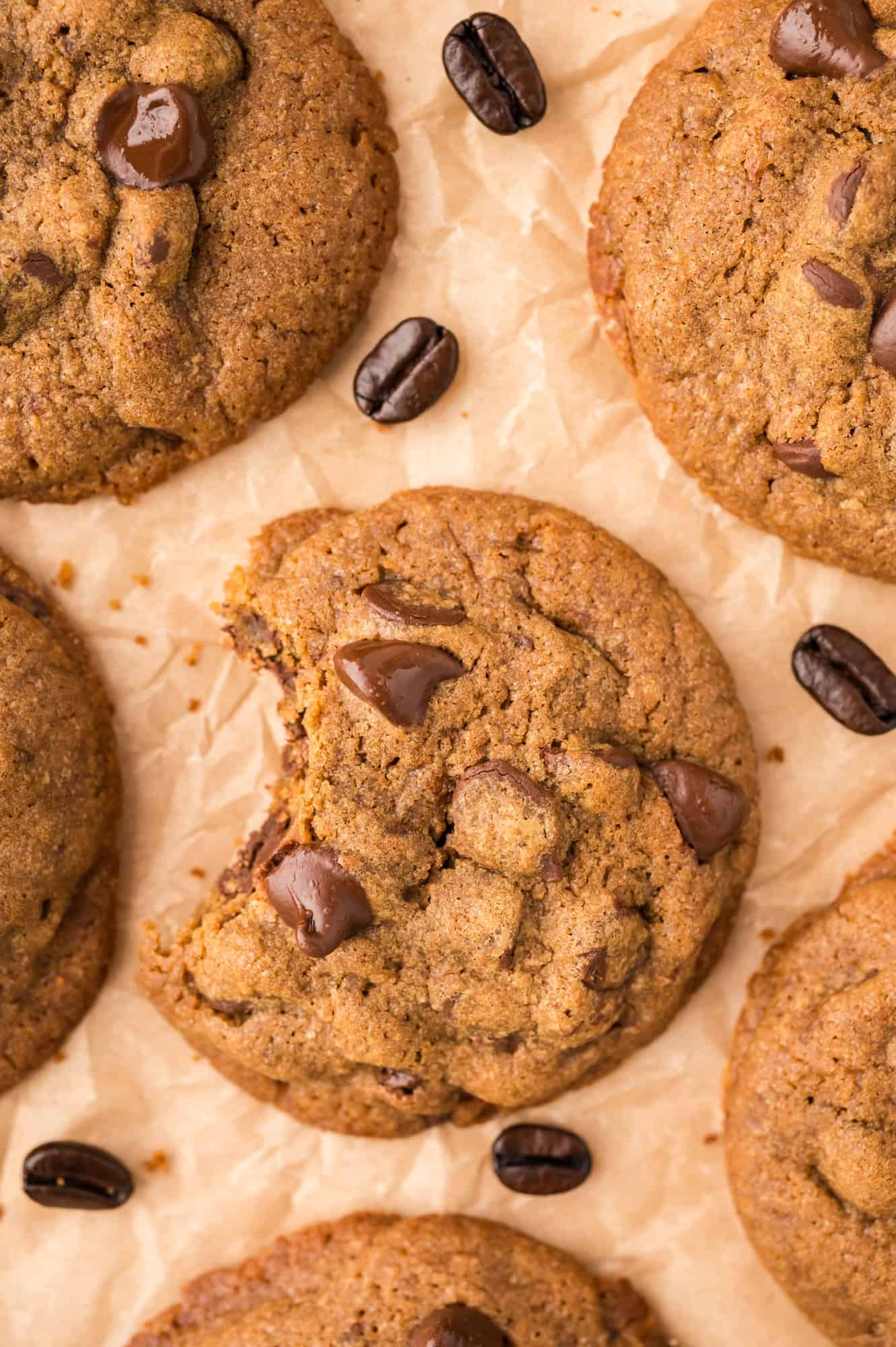 Coffee cookies with chocolate chips, on brown parchment paper, with coffee beans.