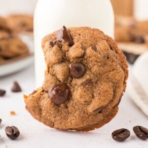Cookie, leaning against milk, with a bite out of it.