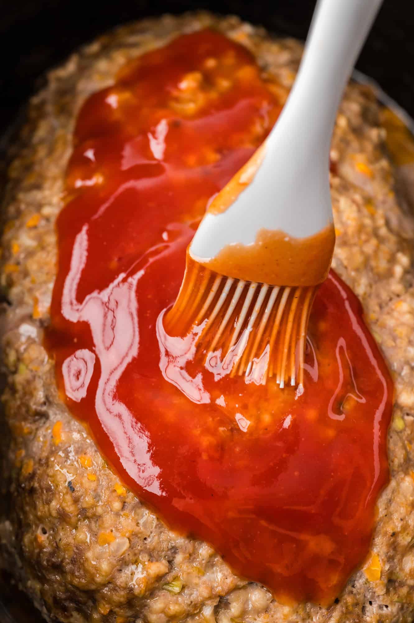 Glaze being brushed on meatloaf.