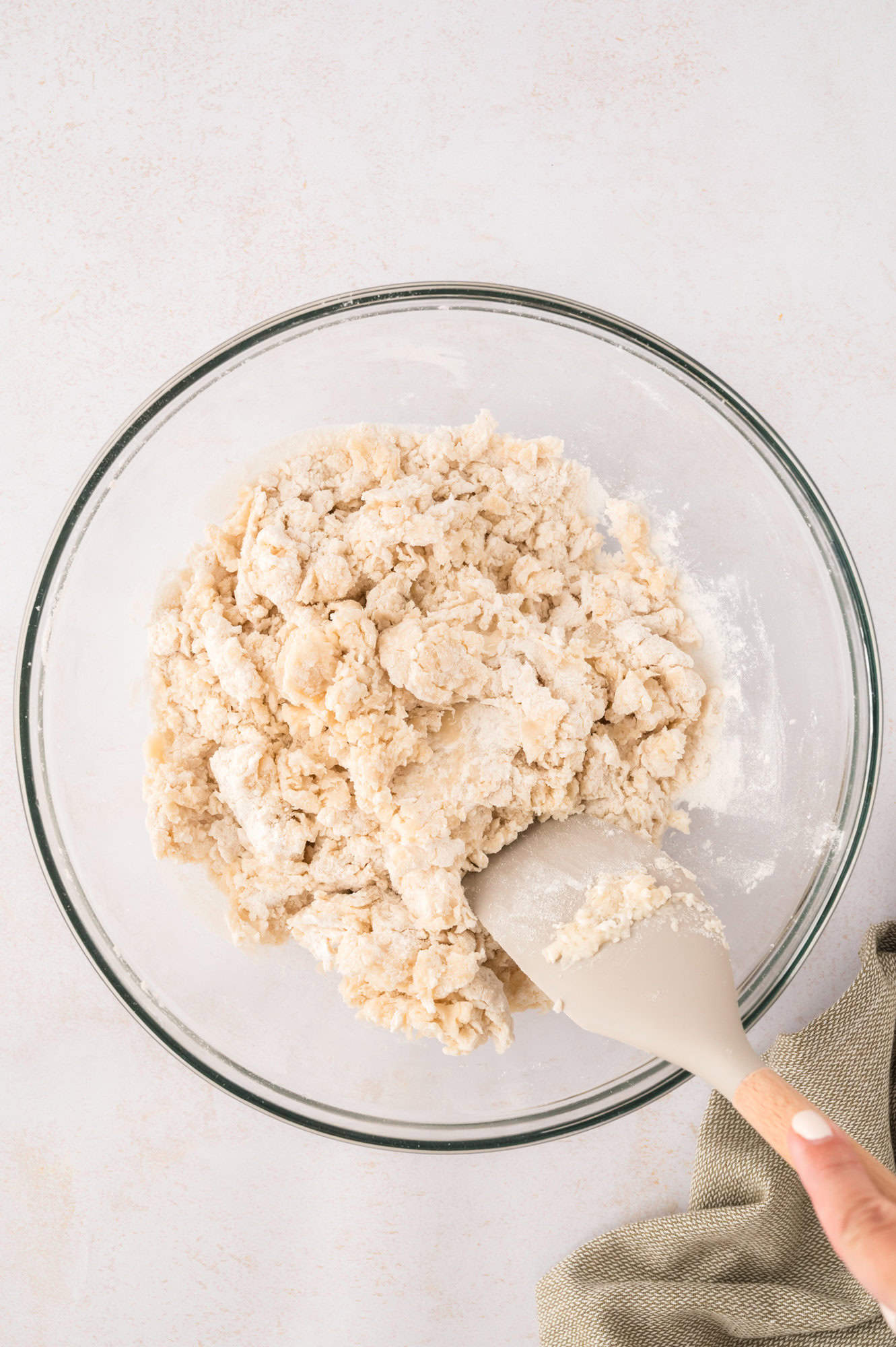 Tortilla dough starting to come together and being stirred with a spatula.