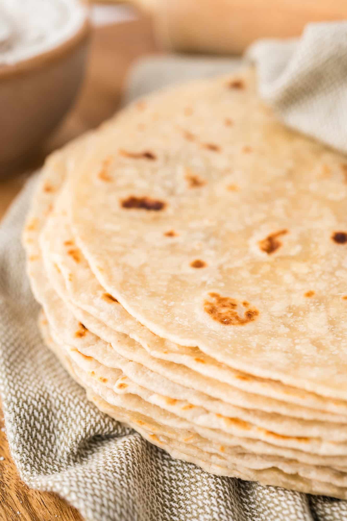 Stack of homemade tortillas partially wrapped in a light green linen cloth.