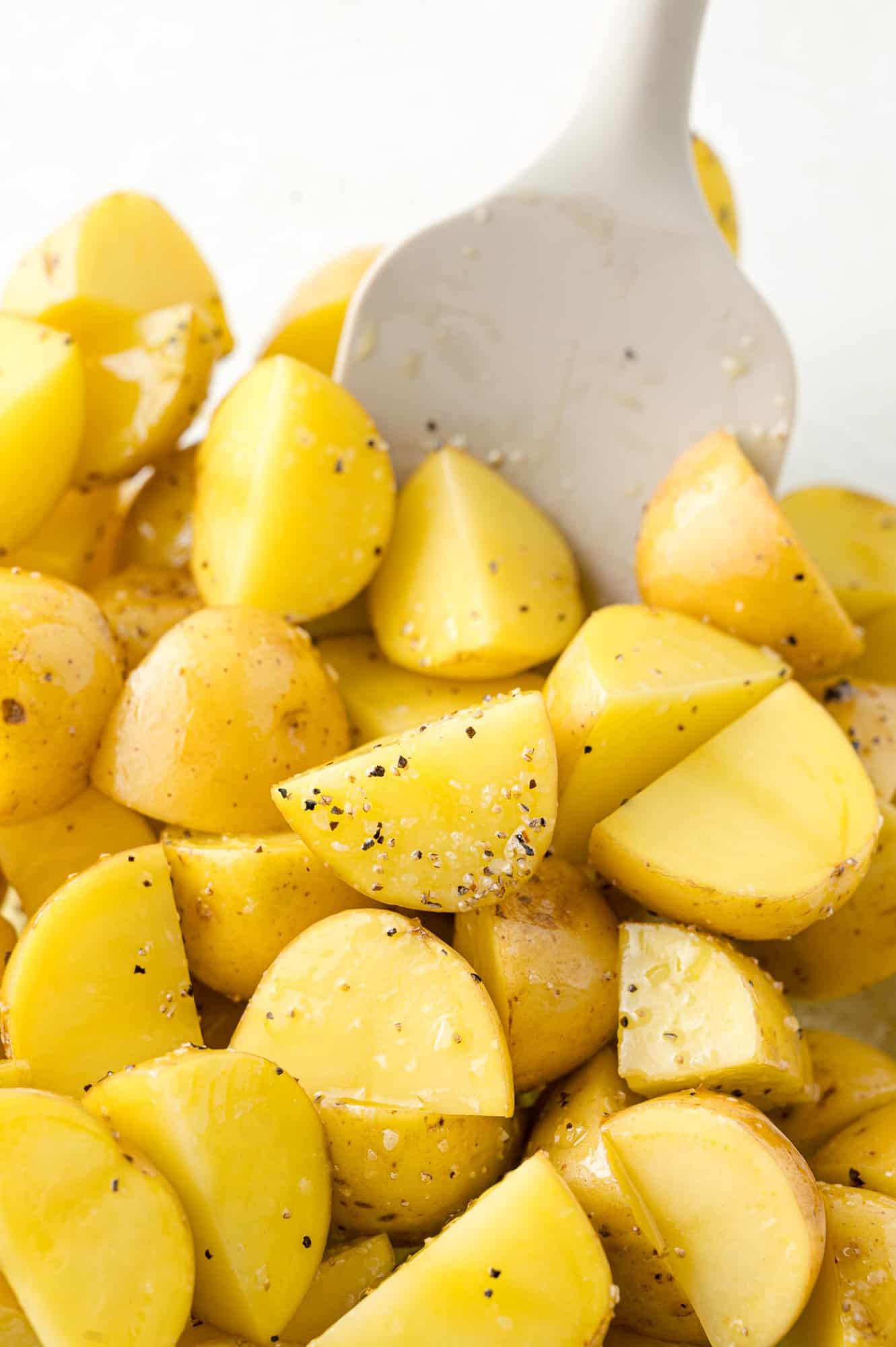 Halved baby potatoes in a clear glass bowl being mixed with salt, pepper, olive oil.