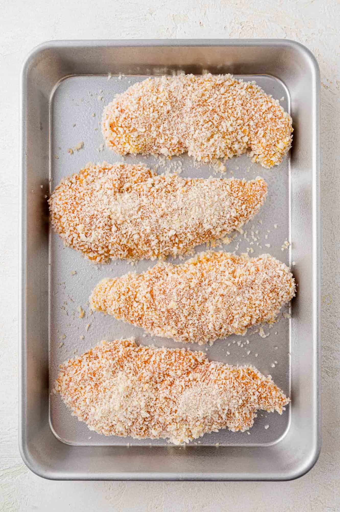 Breaded uncooked chicken tenders on a baking sheet.