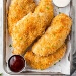 Four golden brown chicken tenders on a tray with ranch and bbq sauce.