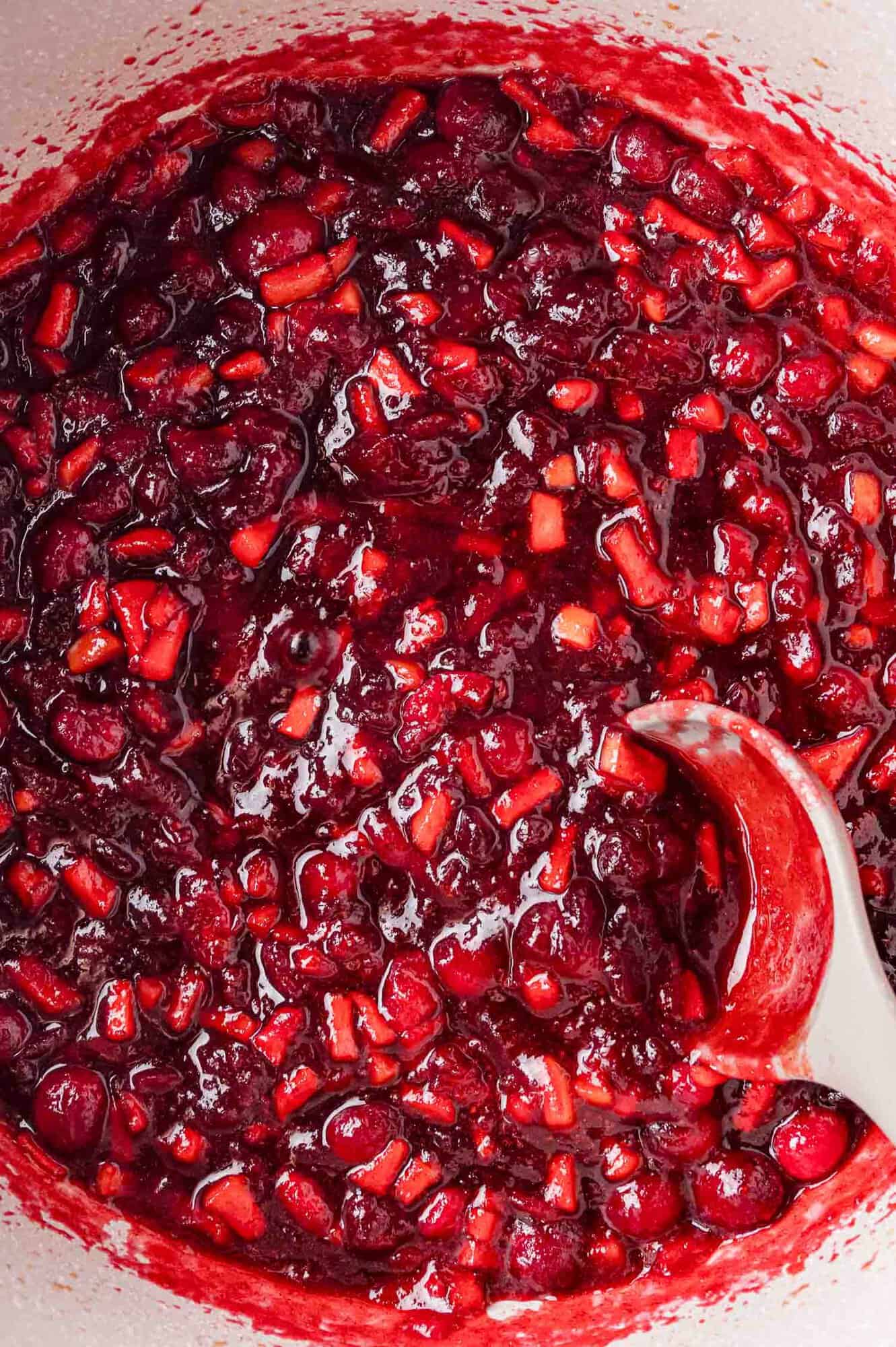 Close-up of a pot filled with chunky cranberry sauce being stirred with a spoon.