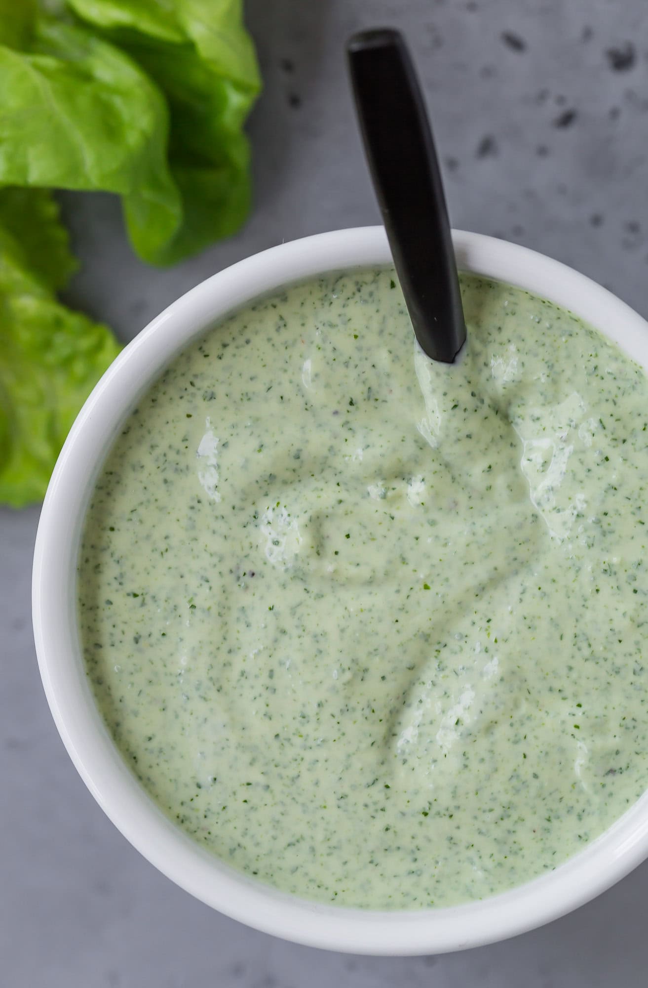 Close up of green goddess dressing in a white bowl.