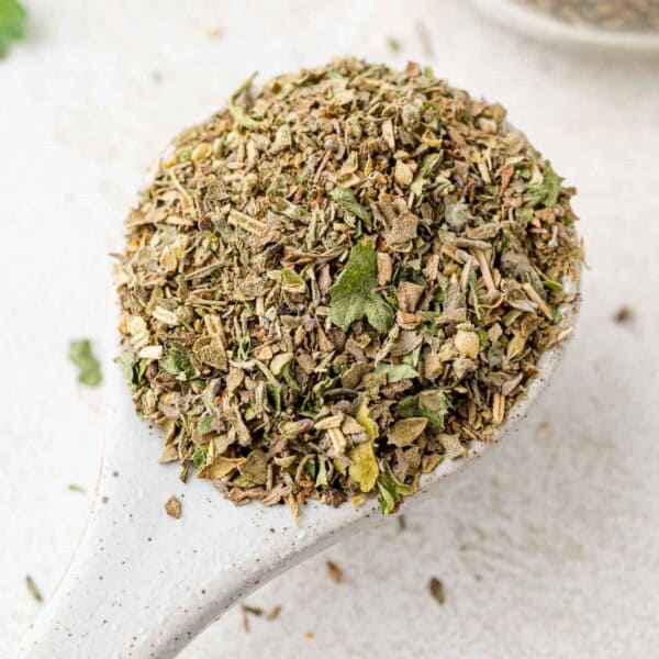 Close up of homemade Italian seasoning on a small white measuring spoon.