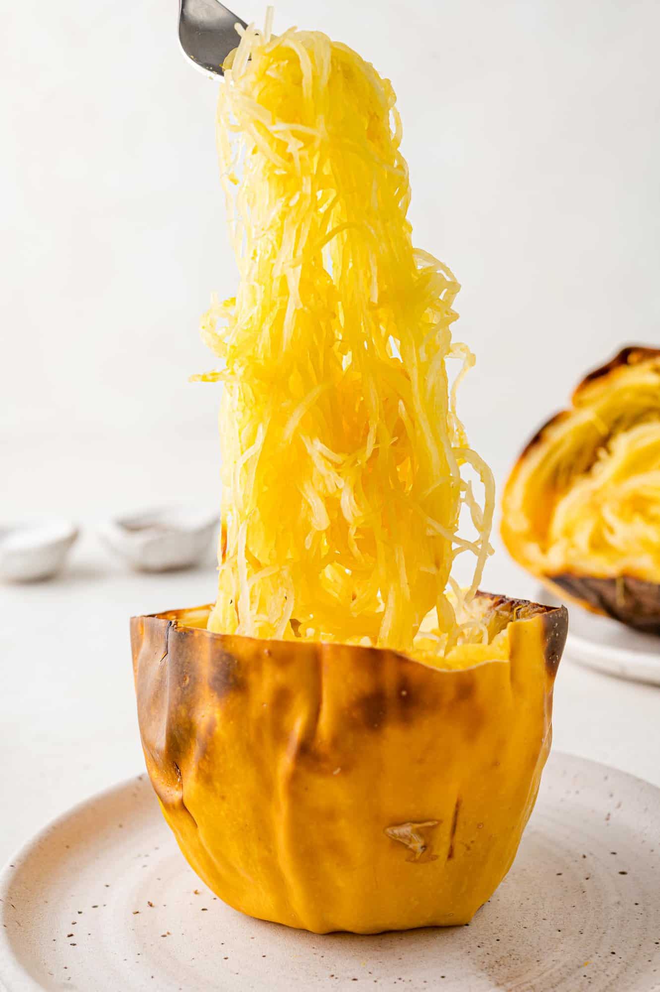 Squash strands being lifted out of spaghetti squash half.