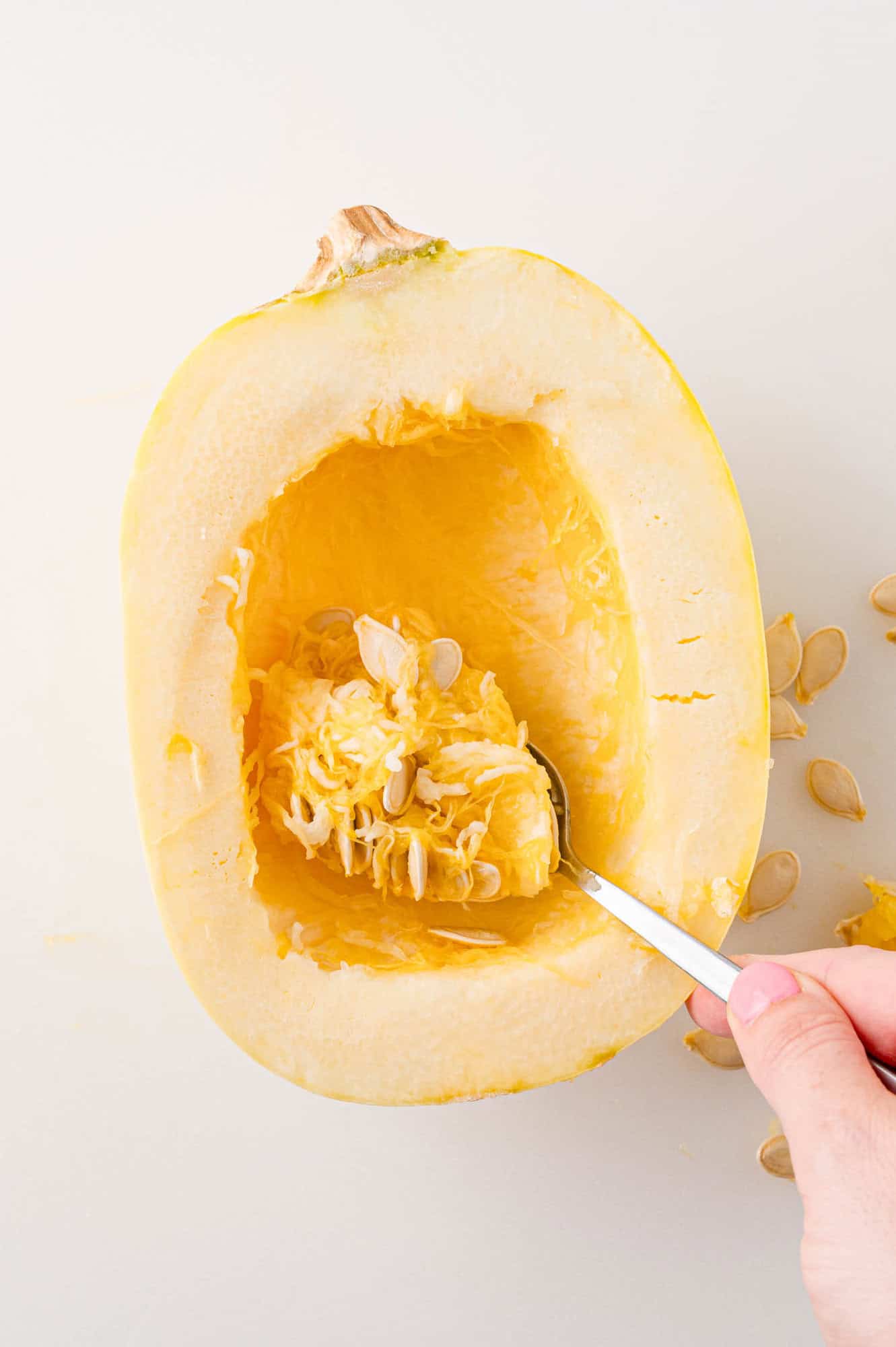 Seeds being scooped out of uncooked spaghetti squash half.
