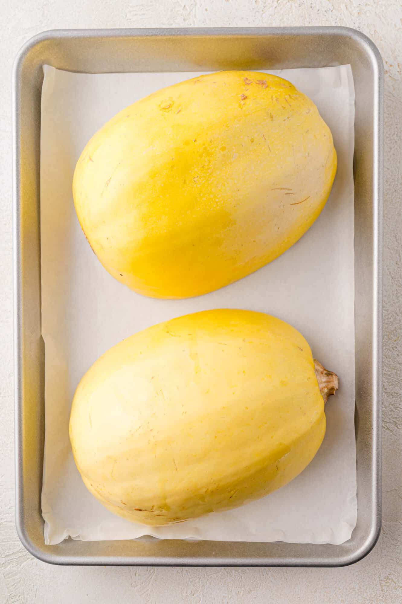 Uncooked squash, face down on baking sheet.
