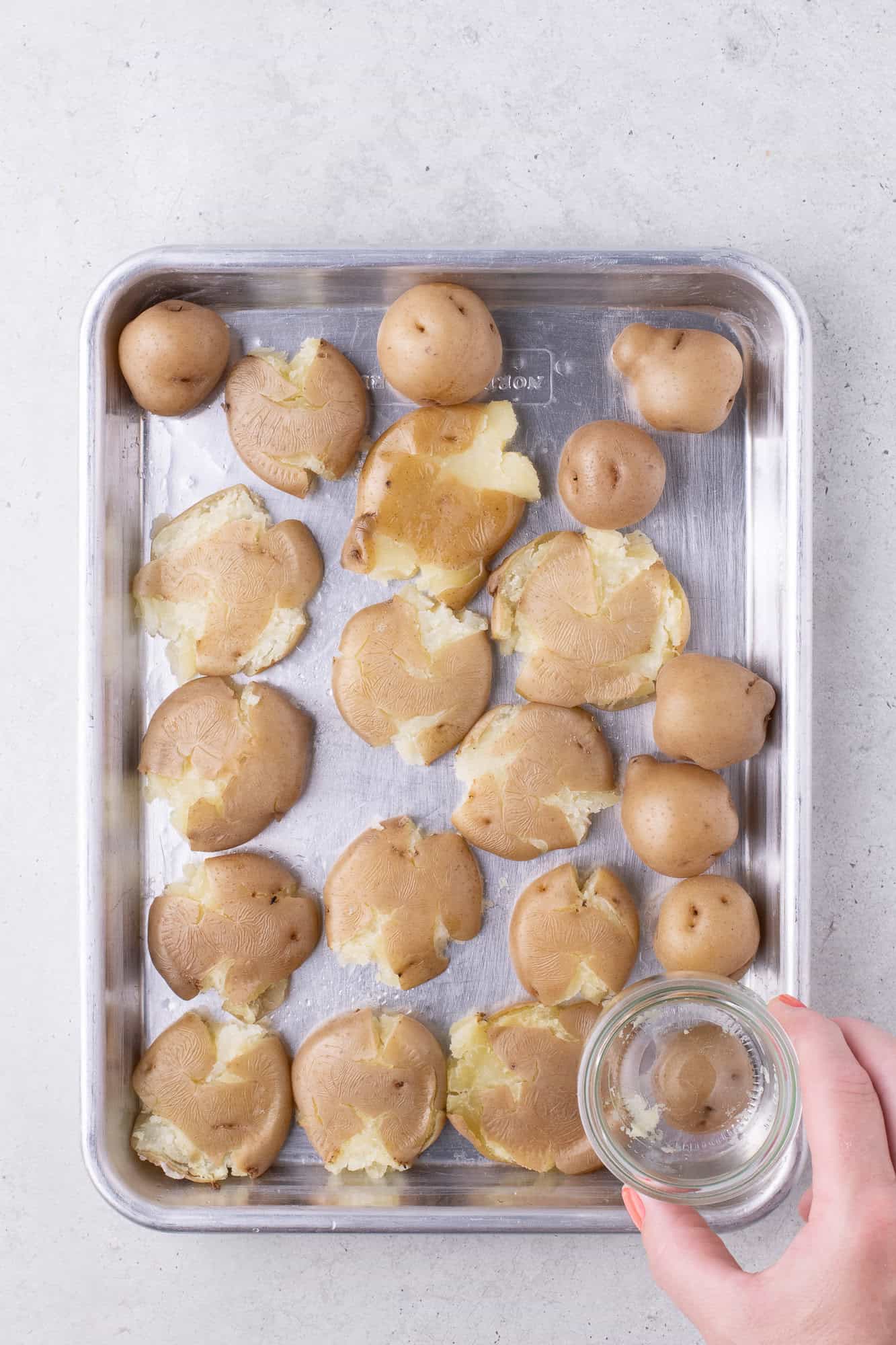 Baby potatoes on a sheet pan, being smashed with a small glass.